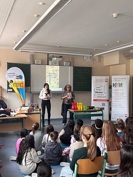 Lesung in Ingolstadt: Mein Papa, die Unglücksspiele und ich

Während der COA‑Aktionswoche las Autorin Gundi Herget gestern an der Grundschule „Auf der Schanz“ in Ingolstadt aus ihrem Buch „Mein Papa, die Unglücksspiele und ich“. Organisiert wurde die Lesung von der Fachstelle Glücksspielsucht der Caritas‑Suchtambulanz Ingolstadt in Kooperation mit der Jugendsozialarbeit an Schulen der Caritas-Kreisstelle Ingolstadt und der Landesstelle Glücksspielsucht in Bayern. Die Aktionswoche wird jährlich von NACOA Deutschland initiiert.

Das Buch erzählt die Geschichte der zehnjährigen Alina, die entdeckt, dass ihr Sparschwein geplündert wird. Gemeinsam mit ihrem Freund Pepe und dessen Detektivkoffer sucht sie nach dem Täter – möglicherweise ihr Vater, der seine Glücksspielsucht finanzieren will.

Herget las mit viel Einfühlungsvermögen und half den rund 75 Kindern der dritten und vierten Klassen, Alinas Gefühle und Herausforderungen nachzuvollziehen. Durch die Zusammenarbeit mit Marie Lehner, Inhaberin der Fachstelle Glücksspielsucht, flossen wichtige Informationen zu pathologischem Glücksspiel ein. Die Lesung war interaktiv gestaltet: Mit Fragen und kurzen Diskussionsrunden wurden die Kinder aktiv einbezogen. Herget vermittelte das schwierige Thema verständlich und zugleich fesselnd.

Im Anschluss stellten die Kinder Fragen und vertieften das Thema weiter. „Die Veranstaltung hat bei den Kindern sicher bleibende Eindrücke hinterlassen. Sie haben erfahren, dass es immer Wege gibt, mit belastenden Situationen umzugehen und Hilfe zu finden“, resümiert Marie Lehner.

Während der COA‑Aktionswoche rücken Kinder aus suchtbelasteten Familien in den Mittelpunkt. Mehr als 2,6 Millionen Kinder in Deutschland sind betroffen. Die Landesstelle Glücksspielsucht in Bayern koordiniert bayernweit Prävention, Forschung, Beratung und Hilfe zum Thema pathologisches Glücksspiel.

Hier erfahren Sie mehr über das Buch, das bei uns kostenlos erhältlich ist: https://www.lsgbayern.de/kinderbuch

Foto: Gundi Herget liest Grundschulkindern aus ihrem Buch. Mit im Bild ist Marie Lehner. Foto: Sandra Daniel/Caritas