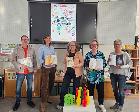 Lesung zum Thema Glücksspielsucht anlässlich des Bayerischen Präventionstags 

Am 12. Oktober hat im Rahmen des Bayerischen Präventionstag in der Schweinfurter Gartenstadt-Grundschule eine Lesung mit der preisgekrönten Autorin Gundi Herget und ihrem Kinderbuch „Mein Papa, die Unglücksspiele und ich“ stattgefunden. 

Erzählt wird in Hergets Buch die Geschichte der zehnjährigen Alina, die zuhause merkt, dass mit ihrem Papa etwas nicht stimmt. Aber niemand erklärt ihr, was los ist. Dann wird auch noch ihr Sparschwein ausgeraubt und Alina geht auf die Suche nach Antworten, bis sie die Geheimnisse gelöst hat.

Die Veranstaltung gestaltete Gundi Herget gemeinsam mit Dagmar Hofmann und Stefan Glos von der Fachstelle für Glücksspielsucht der Diakonie Schweinfurt.

Dank der überaus lebhaften Lesung hingen die Kinder gebannt an den Lippen der Autorin und auch die dazwischen gestellten Fragen brachten viele gestreckte Arme hervor. Im Anschluss wurde durch ein Spiel verdeutlicht, was die Unterschiede zwischen „normalen“ und „(Un)glücksspielen“ sind.

Zudem wurde den Kindern vermittelt, dass sie zurecht auf ihre Gefühle vertrauen und sich entsprechend auch Unterstützung holen dürfen.

Mit ergänzenden Einblicken von Dagmar Hofmann und Stefan Glos aus der Suchtberatung endete der Besuch in einer regen Fragerunde, die die Kinder mit einem ordentlichen Applaus begleiteten.

An der Veranstaltung nahmen die beiden vierten Klassen teil, sodass sich eine ausgesprochen lebhafte Gruppe von knapp 60 Kindern ergab.

Die Lesung wurde von Landesstelle Glücksspielsucht in Bayern (LSG) finanziert. 

Die Bücher stehen sowohl den Schulen als auch Privatpersonen kostenlos (innerhalb Bayerns) zur Verfügung und können hier bestellt werden: 

https://www.lsgbayern.de/infos-materialien/materialien/webshop-lsg

Auf dem Bild von links:
• Stefan Glos, Leiter der Suchtberatungsstelle
• Dagmar Hofmann, Fachstelle Glücksspielsucht der Suchtberatung Schweinfurt
• Gundi Herget, Kinderbuchautorin
• Ulrike Hieronymus, Schulleitung der Schweinfurter Gartenstadt-Grundschule
• Daniela Glos, stellvertr. Schulleitung der Schweinfurter Gartenstadt-Grundschule 

Foto von Marie Glos.